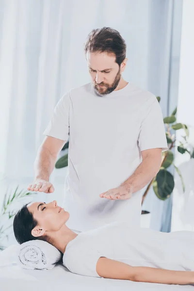 Guérisseur barbu faisant séance de traitement reiki à la jeune femme avec les yeux fermés — Photo de stock