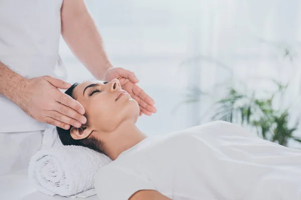 Plan recadré de jeune femme calme avec les yeux fermés recevant un traitement de guérison reiki — Photo de stock