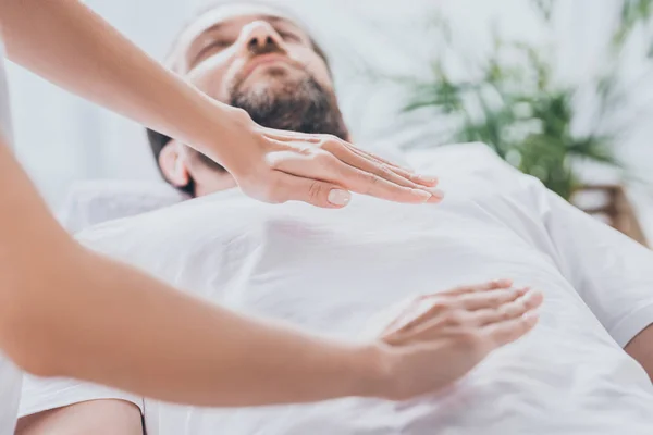 Vista de cerca del hombre barbudo recibiendo sesión de curación de reiki por encima del estómago y el pecho - foto de stock