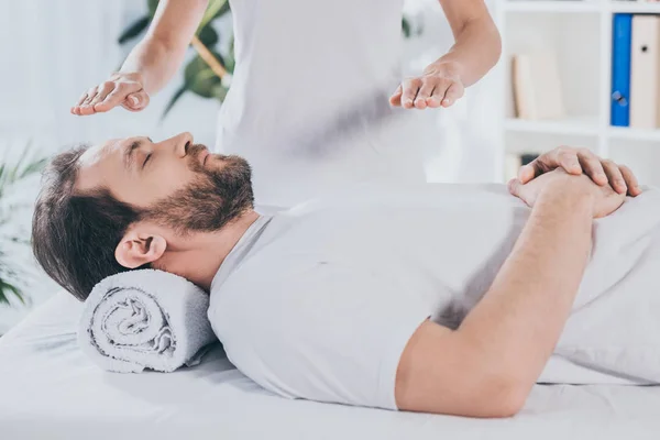 Cropped shot of bearded man with closed eyes receiving reiki treatment — Stock Photo
