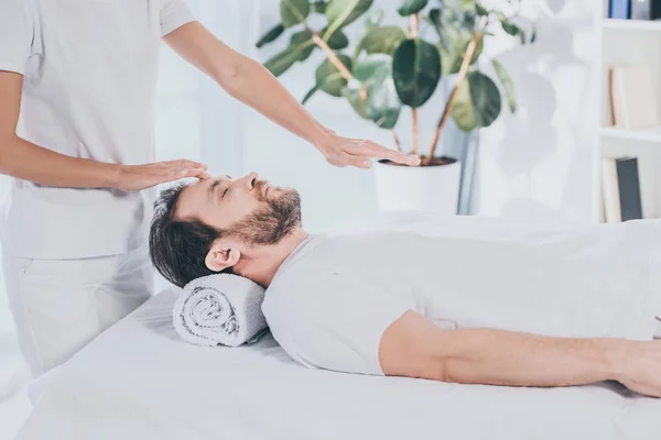 Tiro recortado de curandeiro reiki fazendo sessão de tratamento para acalmar o homem barbudo com os olhos fechados — Fotografia de Stock