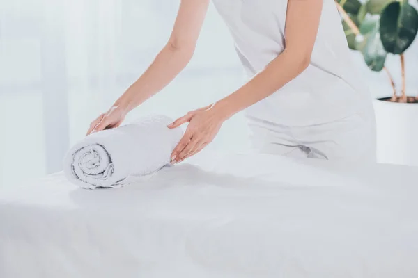 Tiro recortado de trabajador médico poniendo toalla laminada blanca en la mesa de masaje - foto de stock