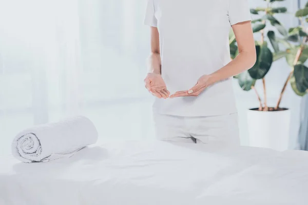 Seção média do curandeiro reiki em pé perto da mesa de massagem branca — Fotografia de Stock