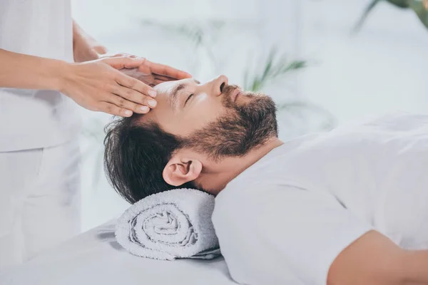 Tiro recortado de especialista reiki fazendo sessão de cura para acalmar o homem barbudo com os olhos fechados — Fotografia de Stock