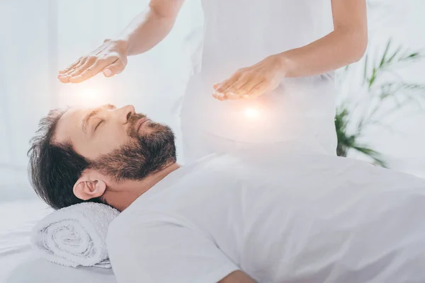 Cropped shot of bearded man with closed eyes receiving reiki healing treatment — Stock Photo