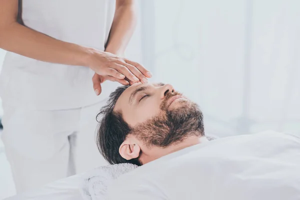 Hombre barbudo tranquilo con los ojos cerrados recibir terapia de curación reiki en la cabeza — Stock Photo