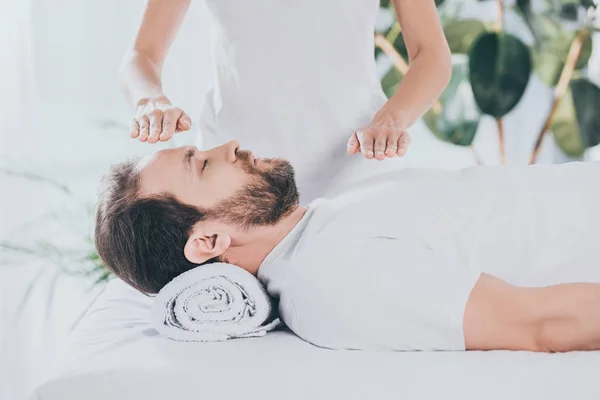 Tiro recortado de hombre barbudo tranquilo con los ojos cerrados recibir terapia curativa reiki - foto de stock