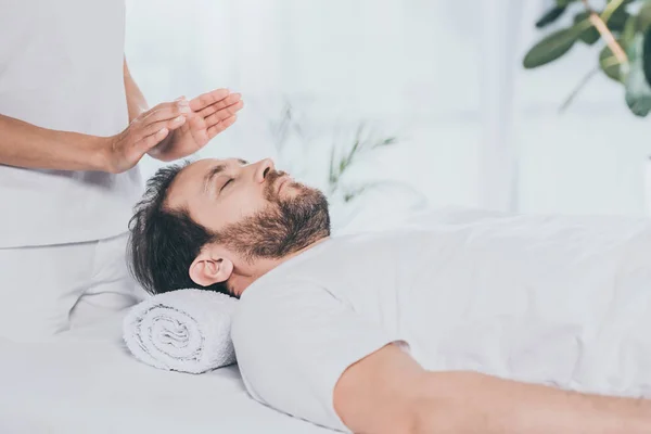 Cropped shot of calm bearded man receiving reiki healing session — Stock Photo