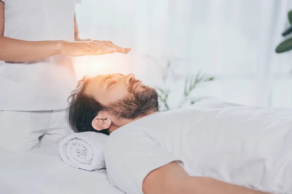 Cropped shot of calm bearded man with closed eyes receiving reiki treatment above head — Stock Photo