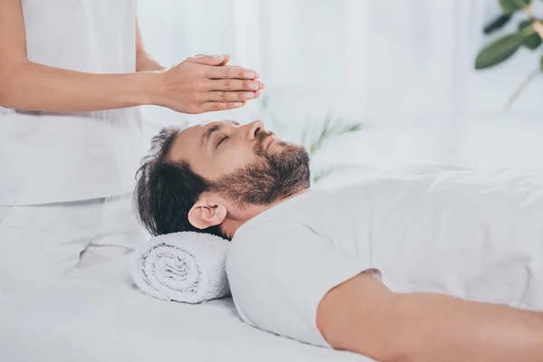 Cropped shot of bearded man with closed eyes receiving reiki treatment above head — Stock Photo