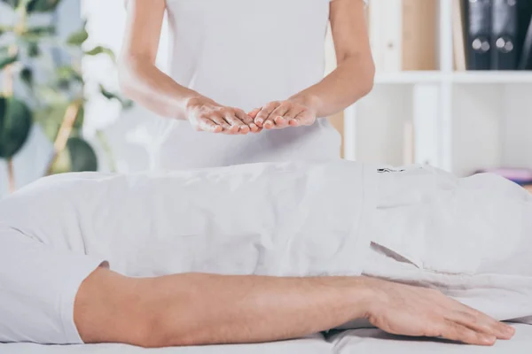 Tiro cortado de homem deitado na mesa de massagem e recebendo tratamento reiki — Fotografia de Stock