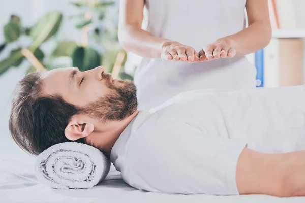 Cropped shot of calm bearded man with closed eyes receiving reiki treatment on chest — Stock Photo