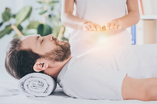 Visão lateral do homem barbudo calmo com olhos fechados recebendo tratamento reiki — Fotografia de Stock