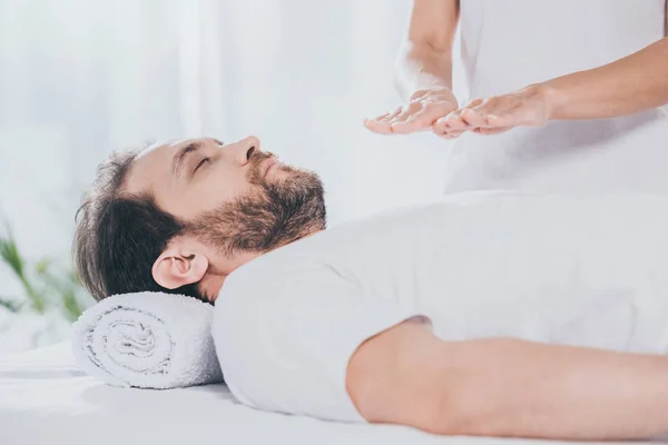 Side view of bearded man with closed eyes receiving reiki treatment on chest — Stock Photo