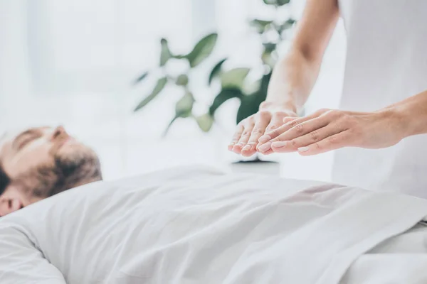 Recortado disparo de barbudo hombre acostado y recibir tratamiento reiki en el estómago - foto de stock