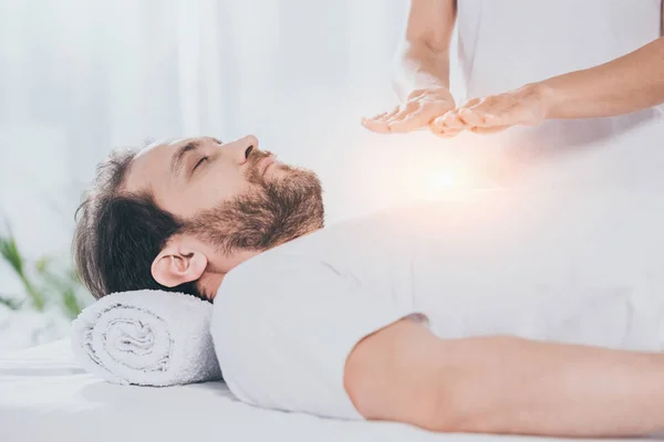 Tiro recortado de homem barbudo com olhos fechados recebendo tratamento reiki no peito — Fotografia de Stock