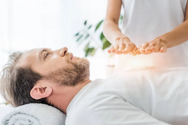 Recortado disparo de barbudo hombre mirando hacia arriba mientras recibe tratamiento reiki - foto de stock