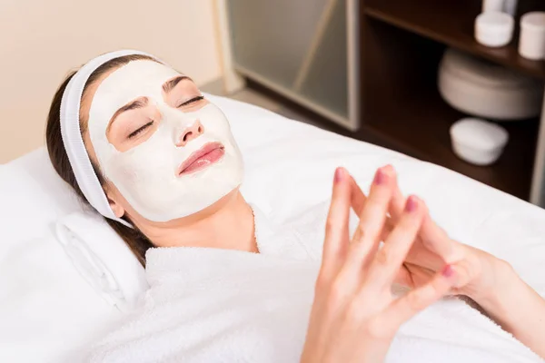 Woman lying in white bathrobe and hairband with applied facial mask at beauty salon — Stock Photo