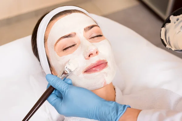 Косметолог наносить косметичну маску на обличчя жінки косметичним пензлем в салоні краси — стокове фото