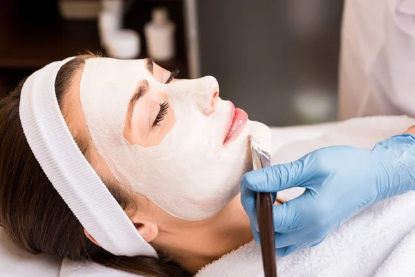 Esteticista aplicando máscara cosmética no rosto da mulher no salão de beleza — Fotografia de Stock