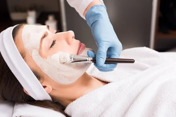 Kosmetikerin trägt Kosmetikmaske auf Gesicht einer Frau im Schönheitssalon auf — Stockfoto