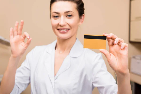 Esteticista mostrando símbolo bien, sonriendo y la celebración de la tarjeta de crédito en el salón de belleza - foto de stock