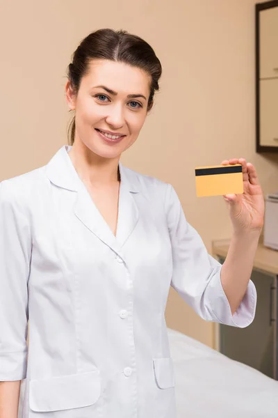 Косметолог тримає кредитну картку і посміхається в салоні краси — стокове фото