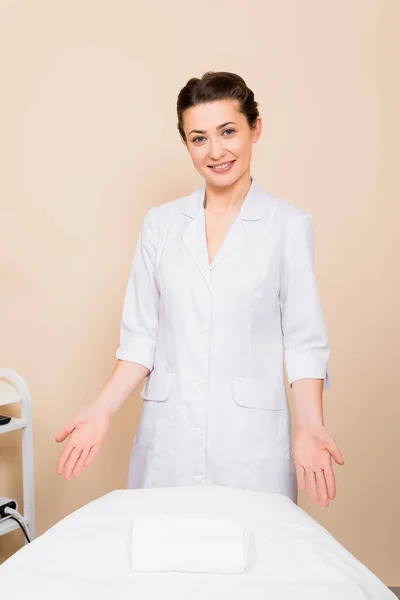 Kosmetikerin steht und zeigt mit den Händen auf Massagetisch im Schönheitssalon — Stockfoto