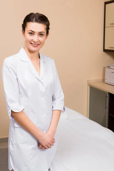 Esteticista de pie cerca del sofá y sonriendo en el salón de belleza - foto de stock