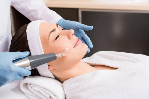 Beautician doing darsonvalization on woman cheek at beauty salon — Stock Photo