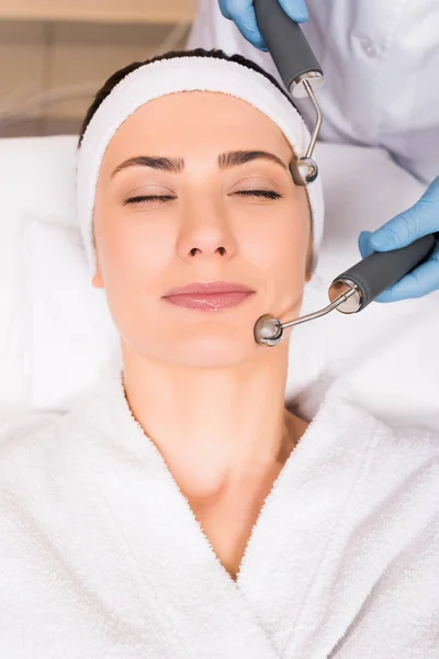 Cosmetologist doing lifting massage on face with equipment to woman at beauty salon — Stock Photo