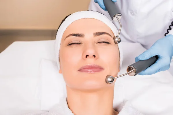 Cosmetólogo haciendo masaje de elevación con equipo en la cara de la mujer en el salón de belleza - foto de stock