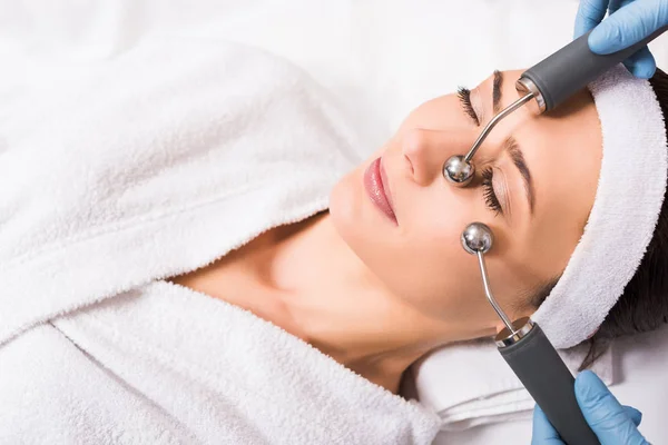 Woman lying wile cosmetologist doing lifting face massage with equipment at beauty salon — Stock Photo