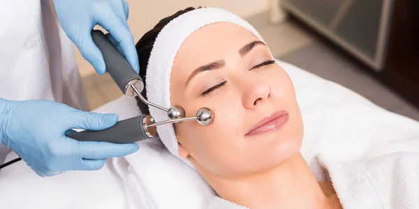 Esteticista fazendo levantamento massagem facial com equipamentos para mulher no salão de beleza — Fotografia de Stock