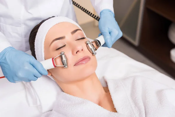 Cosmetologist making massage with equipment on woman face at beauty salon — Stock Photo