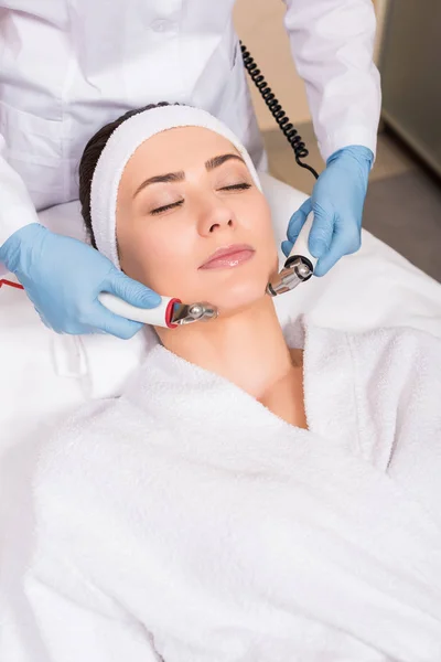 Beautician doing massage with equipment to woman on face at beauty salon — Stock Photo