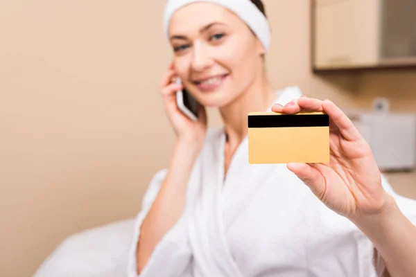 Selective focus of credit card in woman hand, sitting and talking on smartphone at beauty salon — Stock Photo