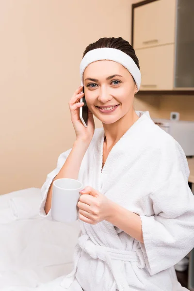 Woman holding cup in hand, talking on smartphone and sitting at beauty salon — Stock Photo
