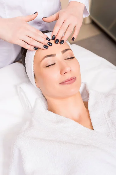 Esteticista dando massagem facial manual para a mulher deitada no salão de beleza — Fotografia de Stock