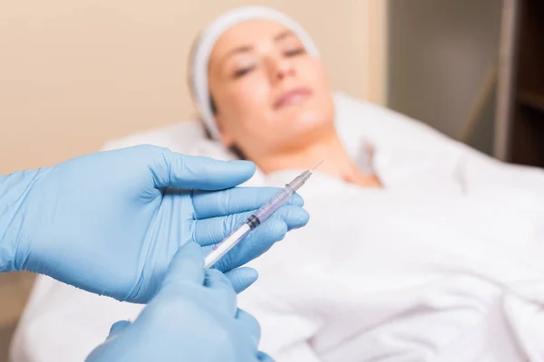 Selective focus of syringe holding by beautician in front of woman face at beauty salon — Stock Photo