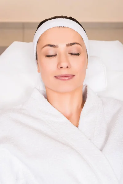 Top view of woman lying in white bathrobe with closed eyes at beauty salon — Stock Photo
