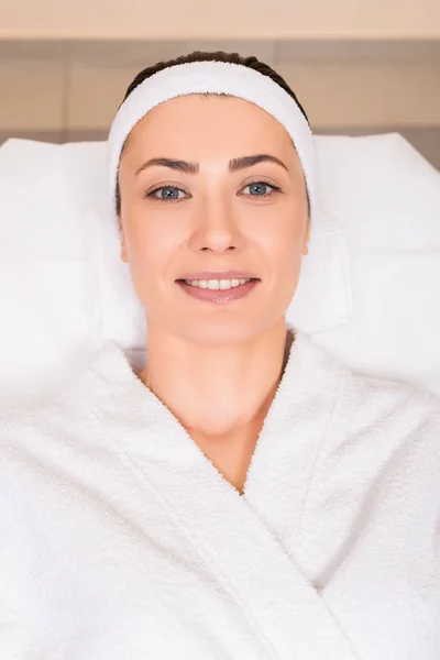 Vista superior da mulher deitada e sorrindo em roupão de banho branco no salão de beleza — Fotografia de Stock