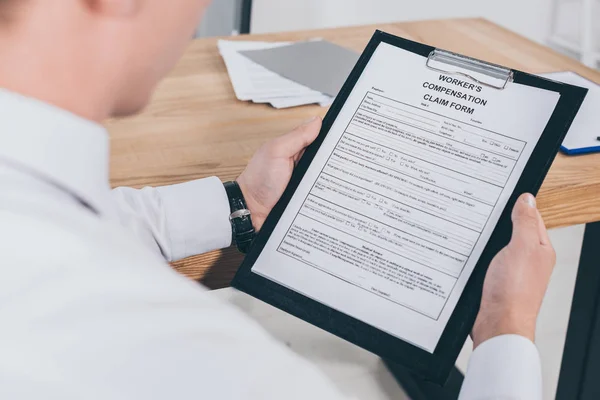 Ausgeschnittene Ansicht eines erwachsenen Geschäftsmannes, der am Arbeitsplatz das Formular für Schadensersatzansprüche liest — Stockfoto