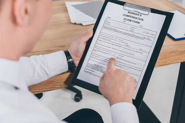 Vista recortada del hombre de negocios lectura formulario de reclamación de indemnización - foto de stock