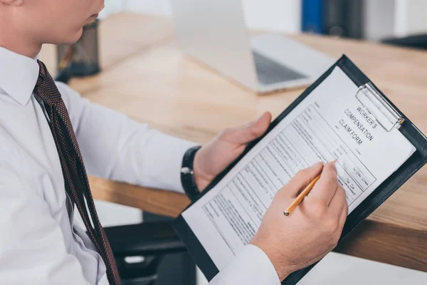 Cropped view of businessman filling in compensation claim form at workplace — Stock Photo