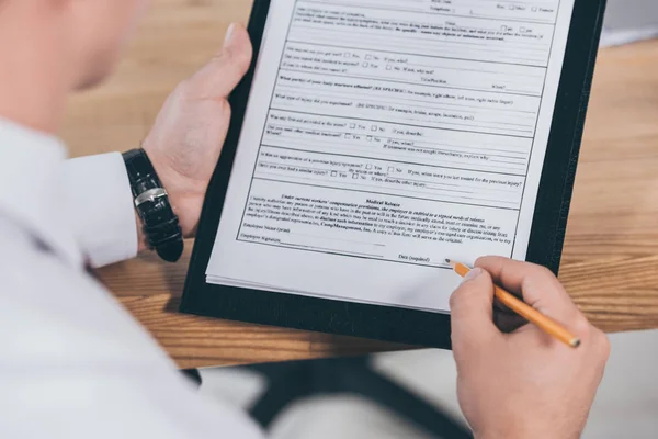 Vista recortada del empresario que firma en el formulario de reclamación de indemnización en el espacio de trabajo - foto de stock