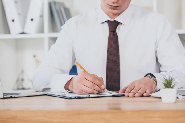 Cropped view of businessman filling in compensation claim at workspace — Stock Photo