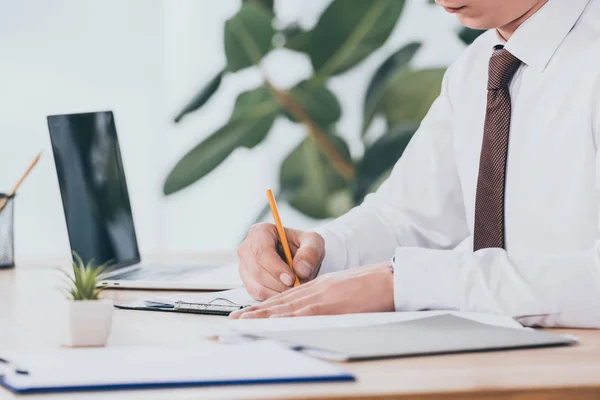 Vista recortada de empresario escribiendo en documento en el lugar de trabajo, concepto de compensación - foto de stock