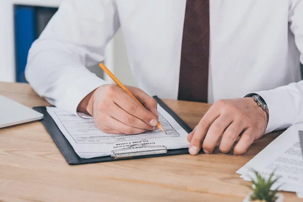 Vista recortada del empresario escribiendo en el formulario de reclamación de indemnización en el lugar de trabajo — Stock Photo