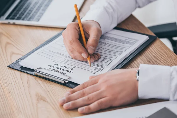 Partial view of businessman filling in compensation claim at workplace — Stock Photo